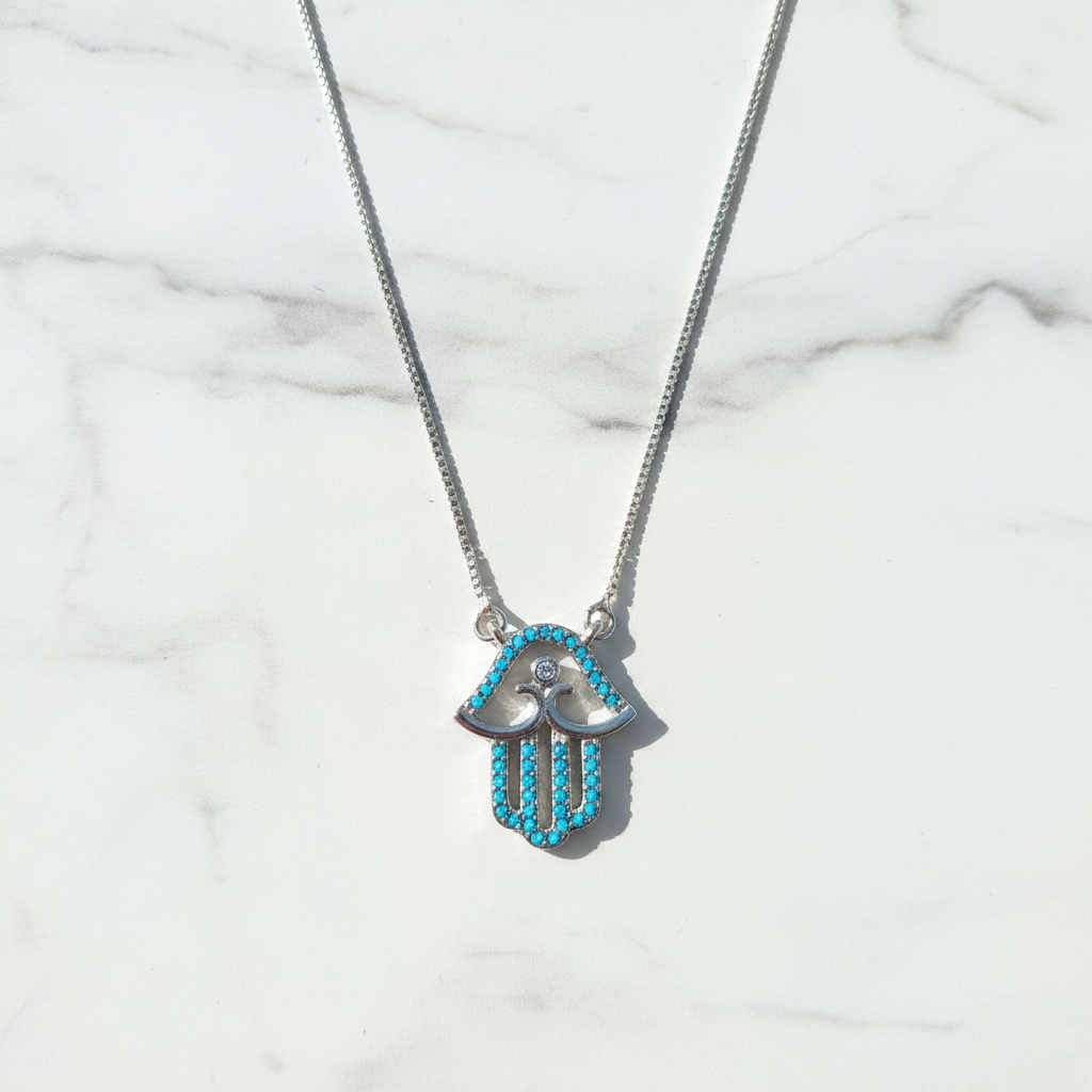 Silver turquoise hamsa necklace on white marble surface overhead shot