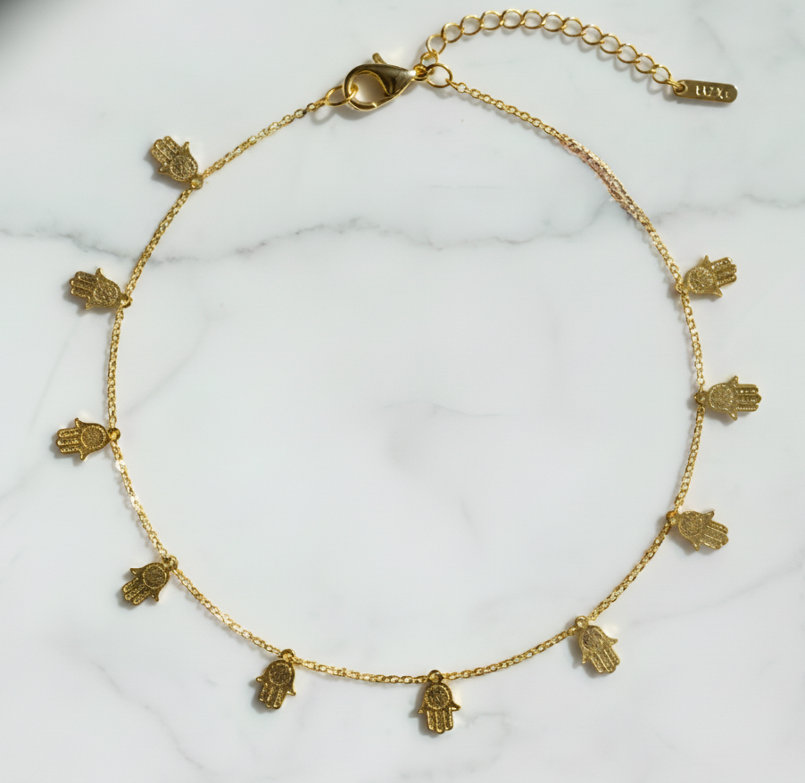 Gold necklace with hamsa hand charms on a white marble surface