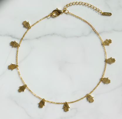 Gold necklace with hamsa hand charms on a white marble surface