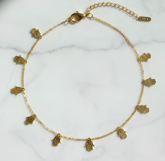 Gold necklace with hamsa hand charms on a white marble surface