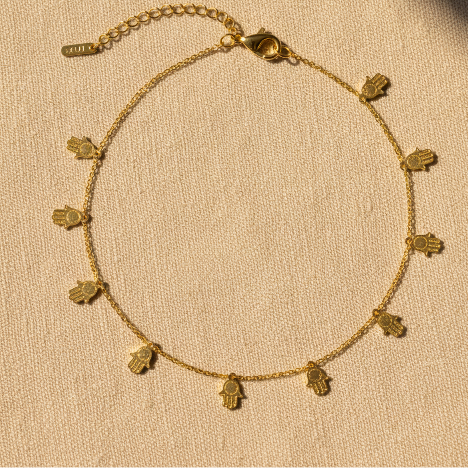 Gold hamsa charm anklet on warm linen background