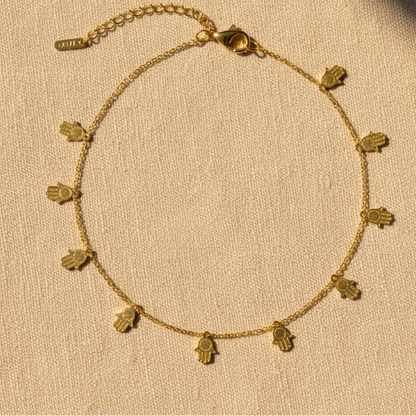 Gold hamsa charm anklet on warm linen background