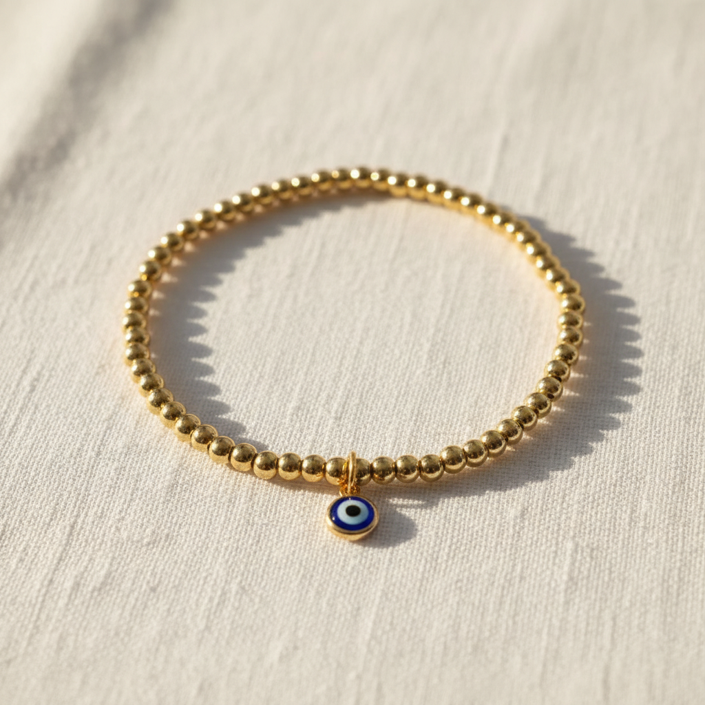 Flat lay of gold beaded evil eye anklet on white linen