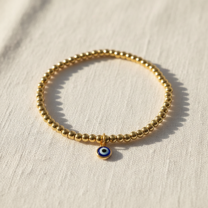Flat lay of gold beaded evil eye anklet on white linen