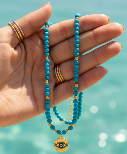 Close-up of turquoise evil eye necklace held in hand with ocean background