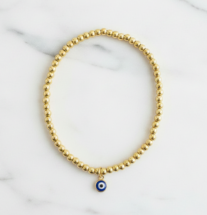 Gold beaded evil eye anklet on white marble surface overhead shot