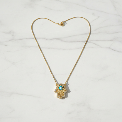 Hamsa evil eye necklace on white marble surface, clean overhead shot