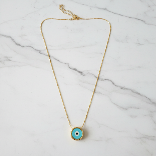 Turquoise evil eye gold necklace on white marble surface overhead showcase