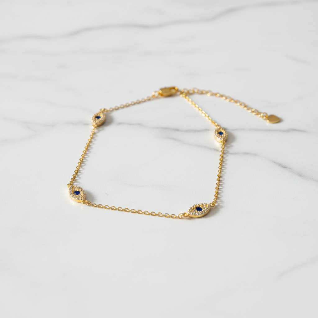 Evil eye gold anklet with pavé crystal charms on white marble surface, clean light background