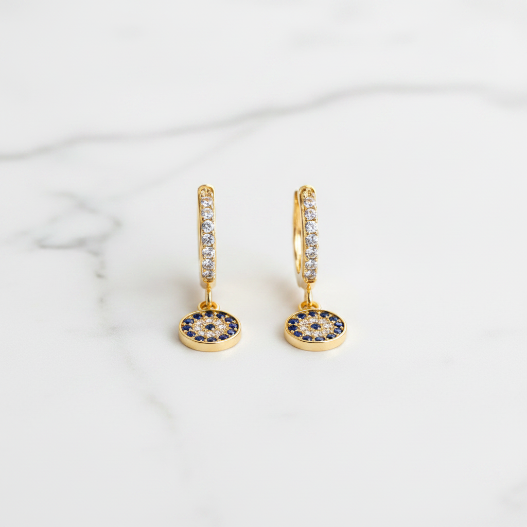 Evil Eye Huggie Drop Earrings on white marble flat lay