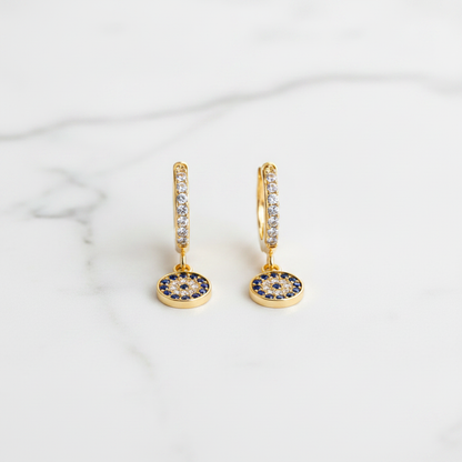 Evil Eye Huggie Drop Earrings on white marble flat lay