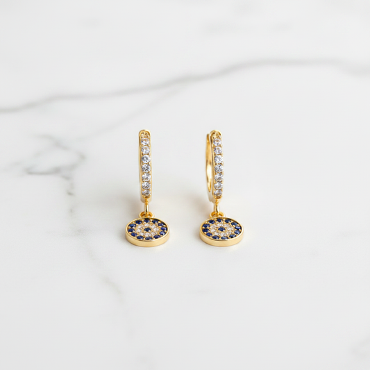 Evil Eye Huggie Drop Earrings on white marble flat lay