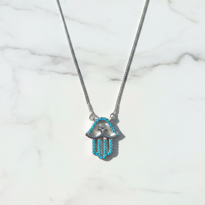 Silver turquoise hamsa necklace on white marble surface overhead shot