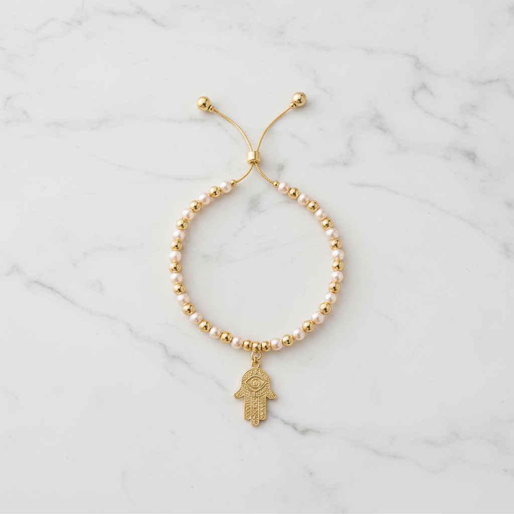 Pearl and gold hamsa bracelet flat lay on white marble background