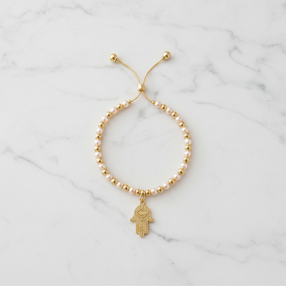 Pearl and gold hamsa bracelet flat lay on white marble background