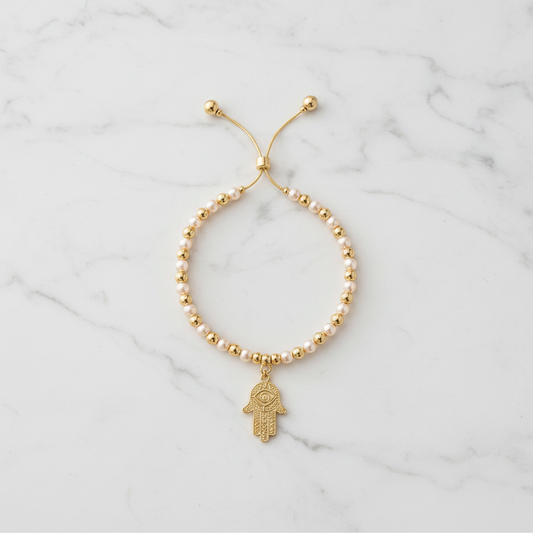 Pearl and gold hamsa bracelet flat lay on white marble background