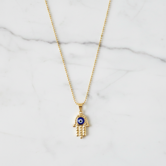 Gold diamond-cut hamsa evil eye necklace on white marble individual showcase