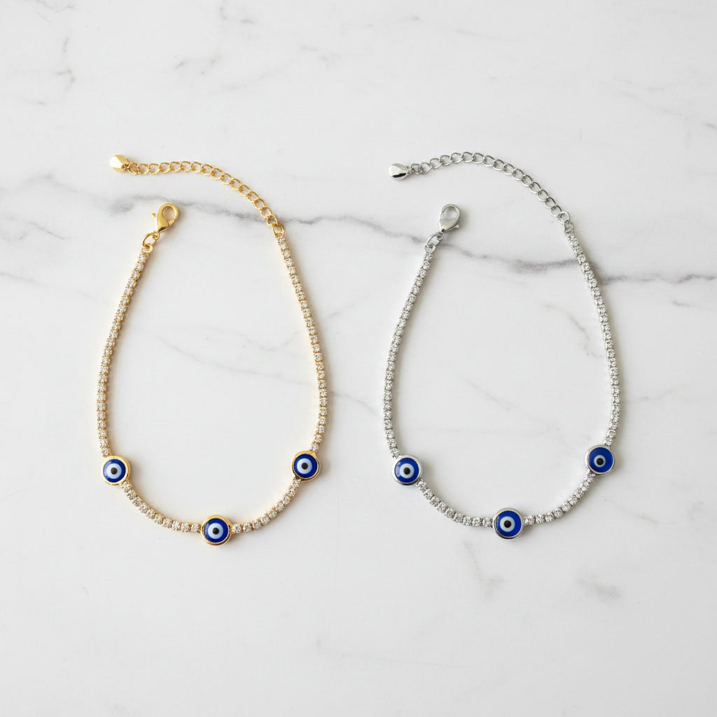 Gold and silver evil eye tennis bracelets side by side on white marble showcase